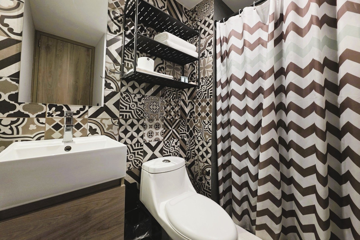 A bathroom with a patterned tile wall, a white sink, and a shower curtain with a zigzag pattern.