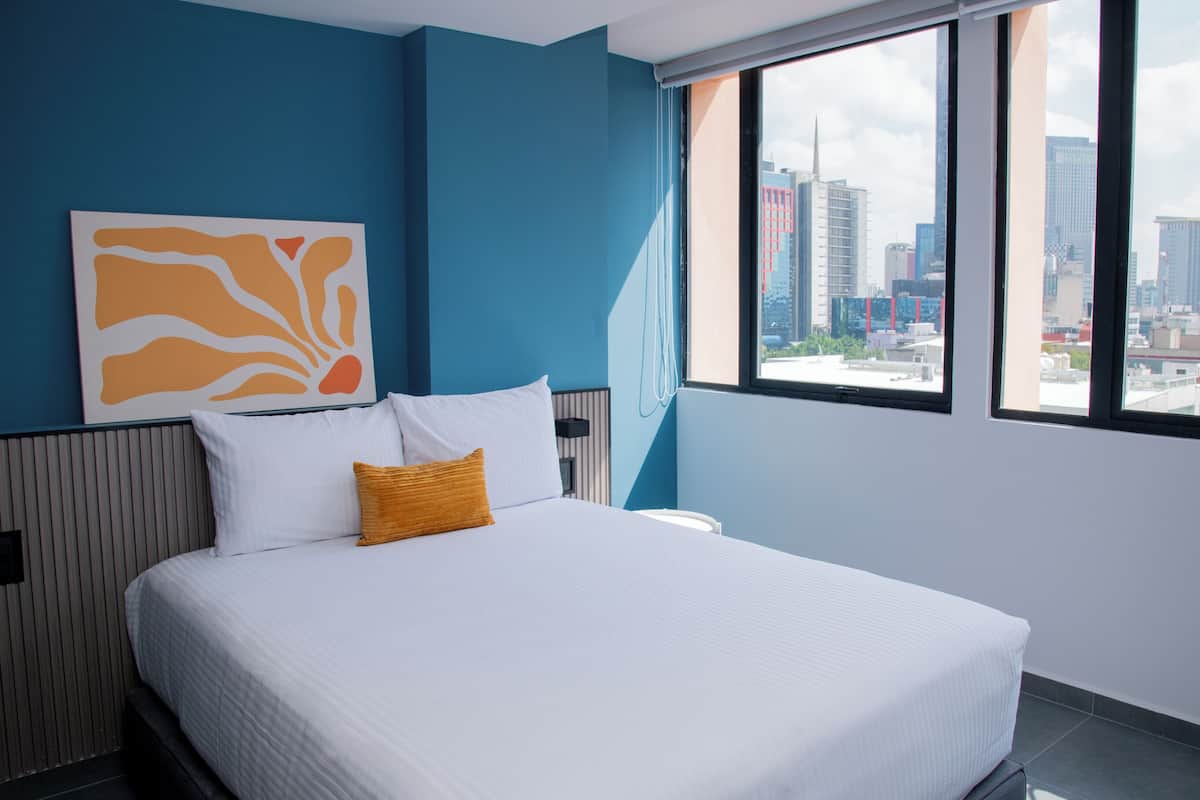 Una habitación de hotel moderna con una cama grande, vistas a la ciudad y un cuadro abstracto único en la pared.