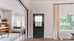 Un salon spacieux avec un piano, un canapé avec une banquette et une grande fenêtre donnant sur un paysage verdoyant.