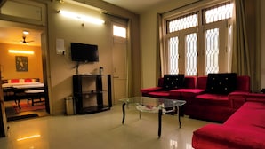 A living room with a glass coffee table, red sofas, a television, and a door leading to a bedroom. - Hotel Cozy Nook (Dalhousie)