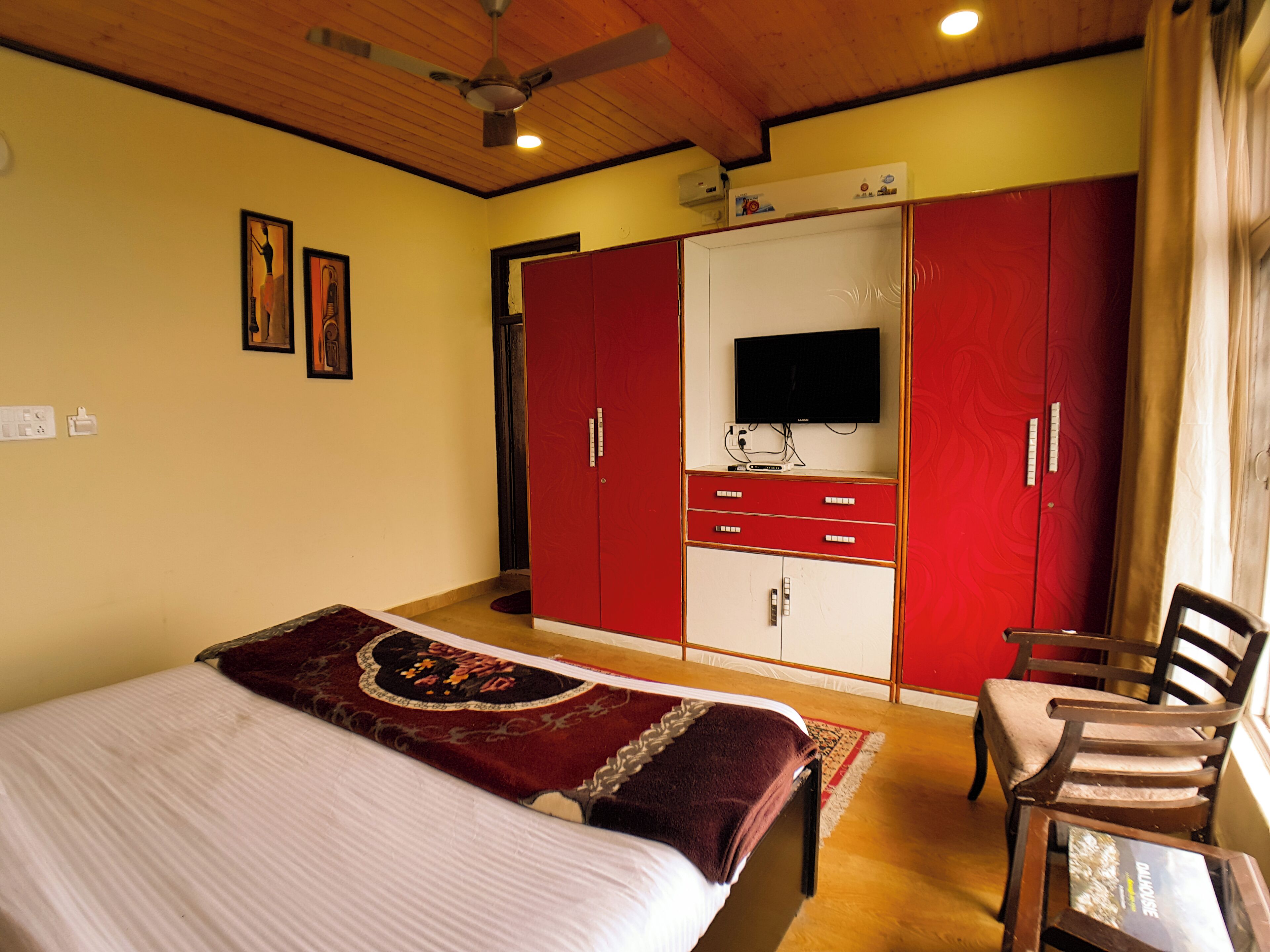 A bedroom with a bed, a TV, a wardrobe, and a chair.