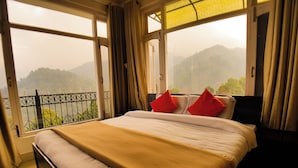 A hotel room with a bed, a view of a mountainous landscape, and a balcony with a railing. - Hotel Cozy Nook (Dalhousie)