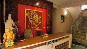 A reception desk with a 'RECEPTION' sign, a statue, and a large decorative wall piece. - Hotel Cozy Nook (Dalhousie)