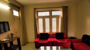 A living room with a red sofa, a glass coffee table, a TV, and a window with decorative bars. - Hotel Cozy Nook (Dalhousie)