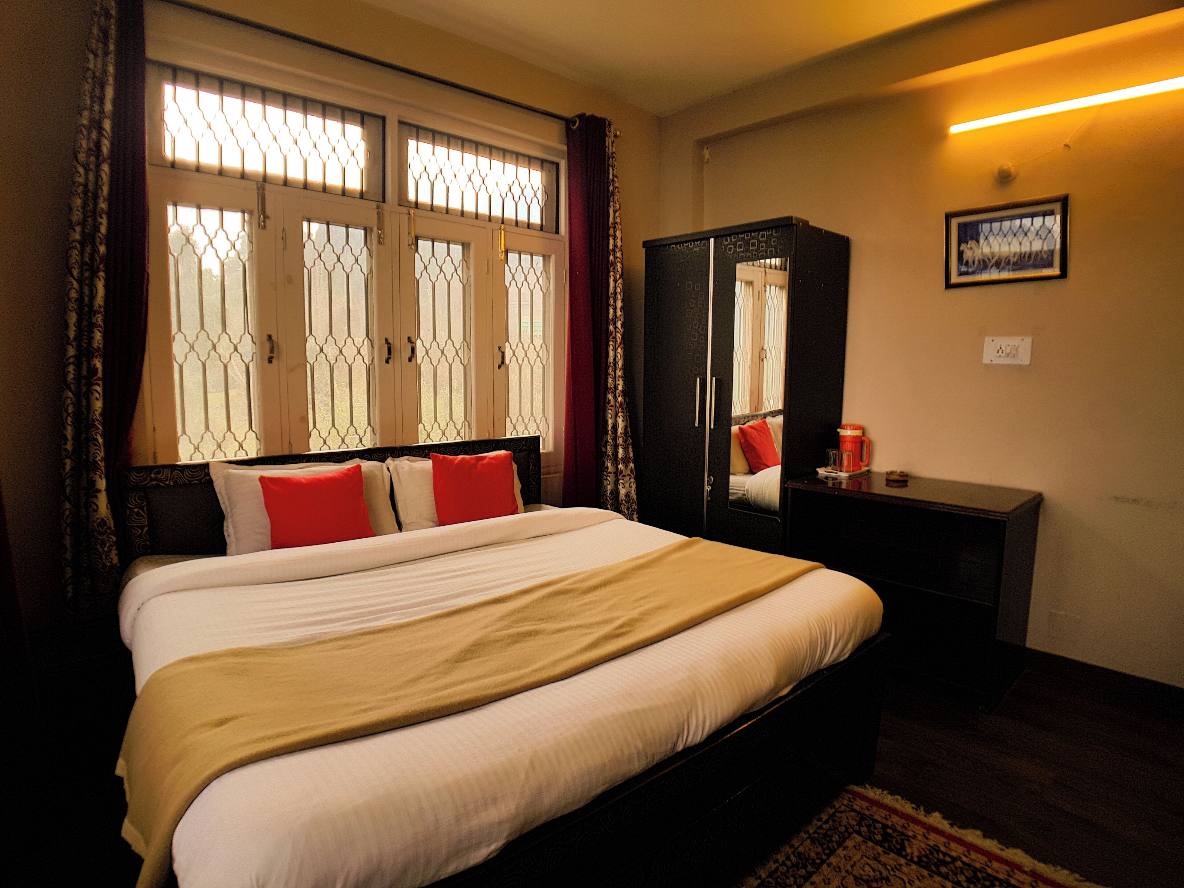 A hotel room with a bed, a wardrobe, a bedside table with a coffee maker, and a window with decorative bars.