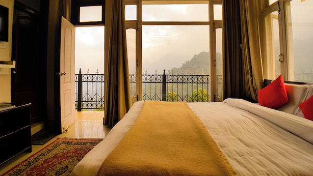 A hotel room with a bed, a TV, and a balcony with a view of the mountains. - Hotel Cozy Nook (Dalhousie)