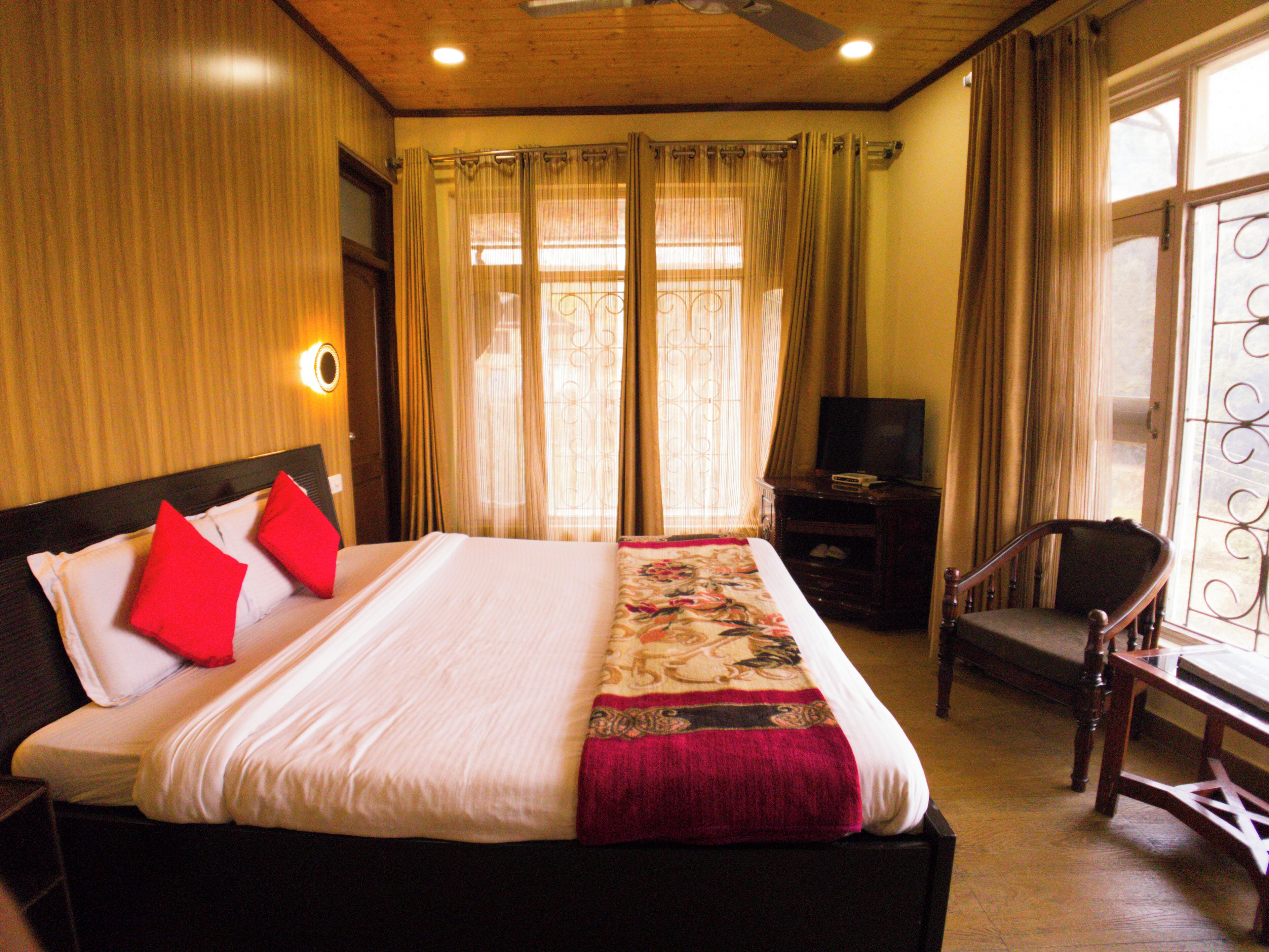 A hotel room with a large bed, a TV, a chair, and curtains.