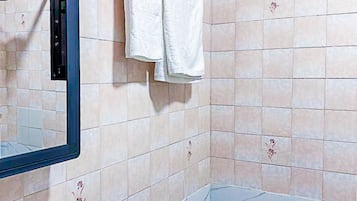 Une salle de bain avec un lavabo blanc, un miroir et un porte-serviettes sur lequel sont posées deux serviettes blanches. Les murs sont recouverts de carreaux décorés d’un motif floral.