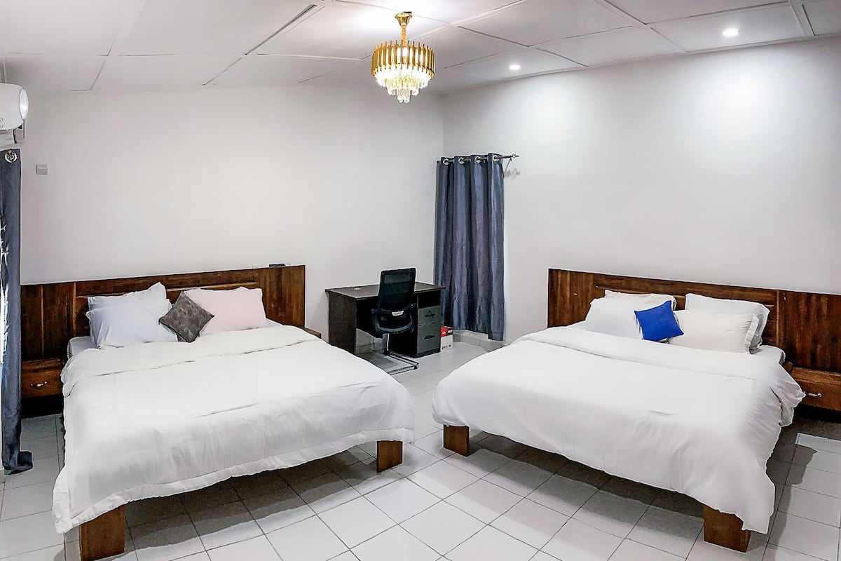 Hotellihuone, jossa on kaksi erillistä sänkyä, työpöytä, tuoli, pieni pöytä ja kattokruunu.