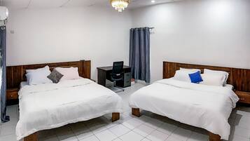 A hotel room with two single beds, a desk, a chair, a small table, and a chandelier.