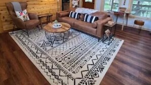 A cozy living room with a wooden ceiling, a brown leather sofa, a patterned rug, and a ceiling fan.