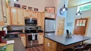A kitchen with wooden cabinets, stainless steel appliances, a central island with bar stools, and pendant lighting.