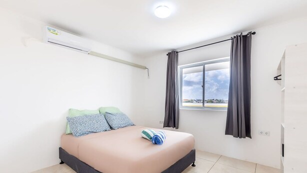 A bedroom with a bed, a window with curtains, an air conditioning unit, and a view of the outside. - Genesis Apartments in Jan Thiel - Swimming Pool (Willemstad)