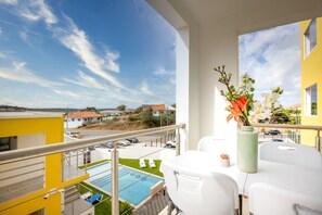 Ein Balkon mit Pool, weißen Möbeln und einem Blumenstrauß.