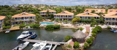 Ein Küstenresort mit mehreren Villen, einer Marina mit Booten, einem Schwimmbad und üppiger Vegetation.