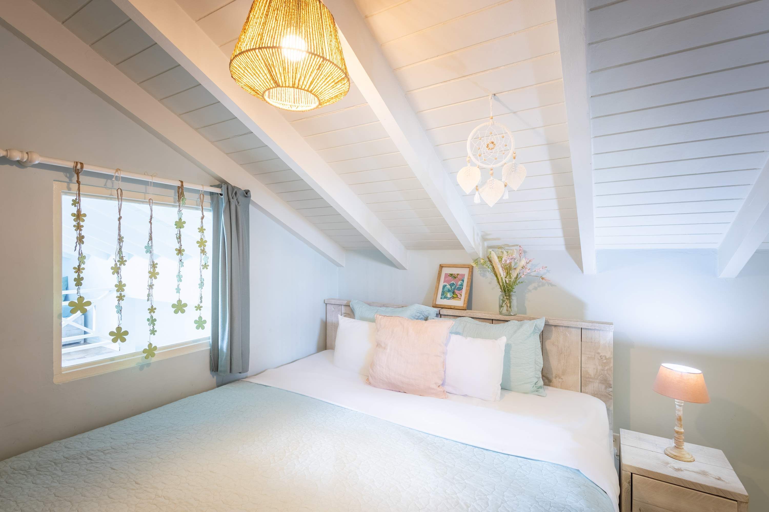 Ein Schlafzimmer mit Bett, Nachttisch, hängenden Dekorationen und einer Deckenleuchte.