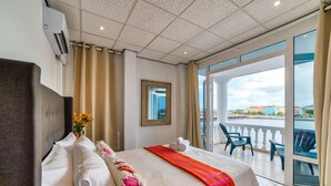 A hotel room with a large bed, a view of the city, and a balcony with chairs. - Stunning Balcony View Spacious 2BR Apt at Unique Location (Willemstad)