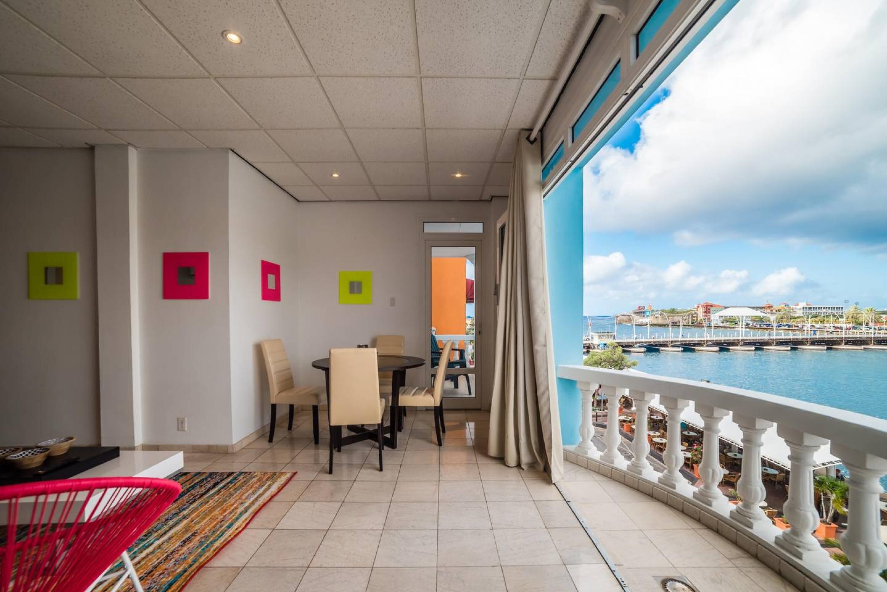 Ein Balkon mit Meerblick, ein Essbereich mit Stühlen und einem Tisch sowie ein Zimmer mit Fenster zum Meer.