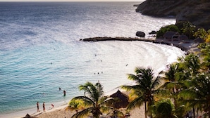 A beach with clear turquoise water, palm trees, and a rocky outcrop. - Blue Bay The Reef Balcony (Sint Michiel)