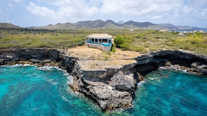 A coastal property with a house on a cliff overlooking turquoise waters and a mountainous landscape. - Cliff Villa - Award Winning Luxury Retreat (Sabana Westpunt)