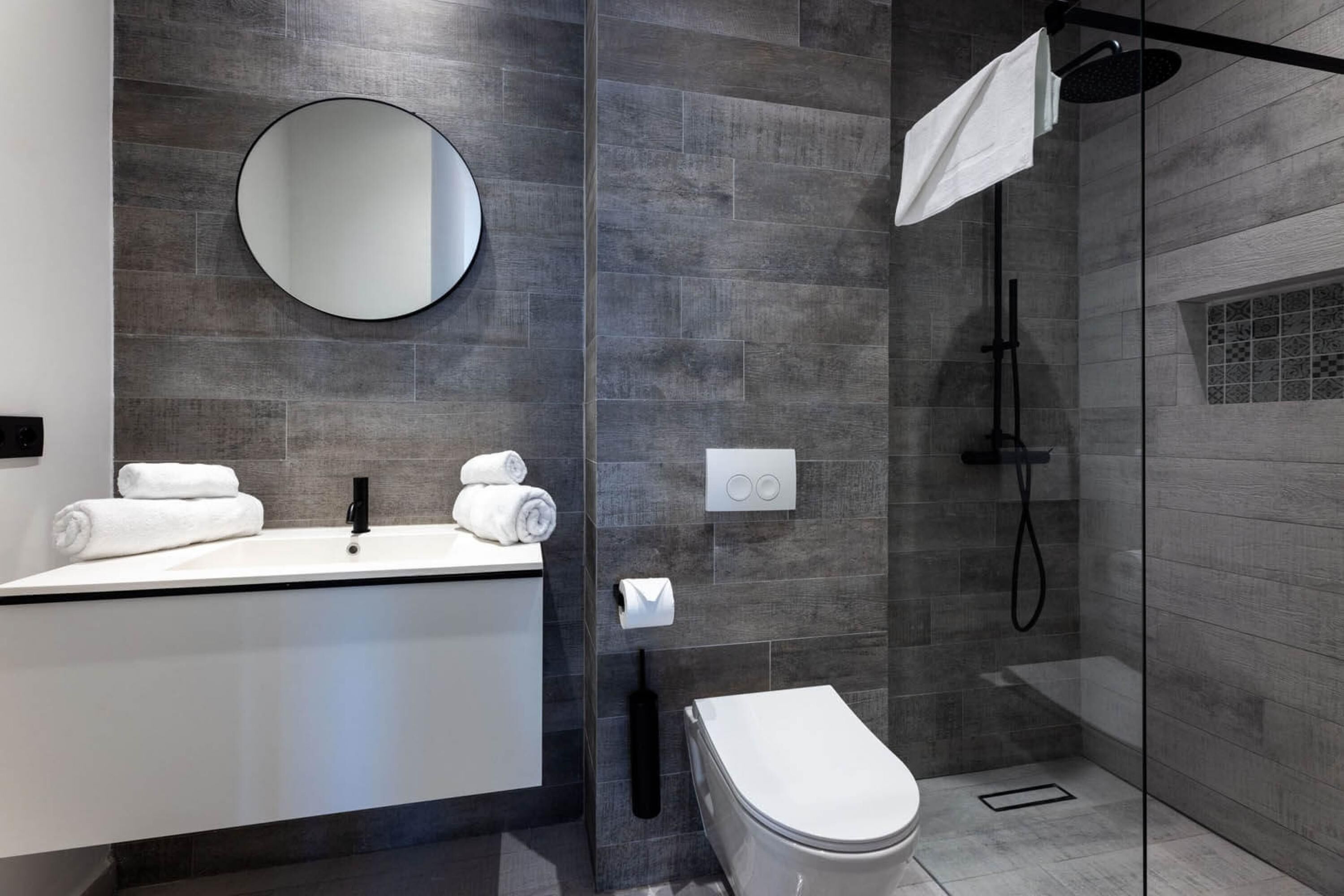 Une salle de bain moderne avec un grand miroir, un lavabo blanc, des toilettes et une douche séparée par une paroi de verre.