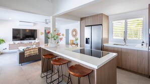 A modern kitchen with a central island, bar stools, a refrigerator, and a large window with blinds. - 270 Ocean Views From Private Pool Sun Terrace (St. Marie)
