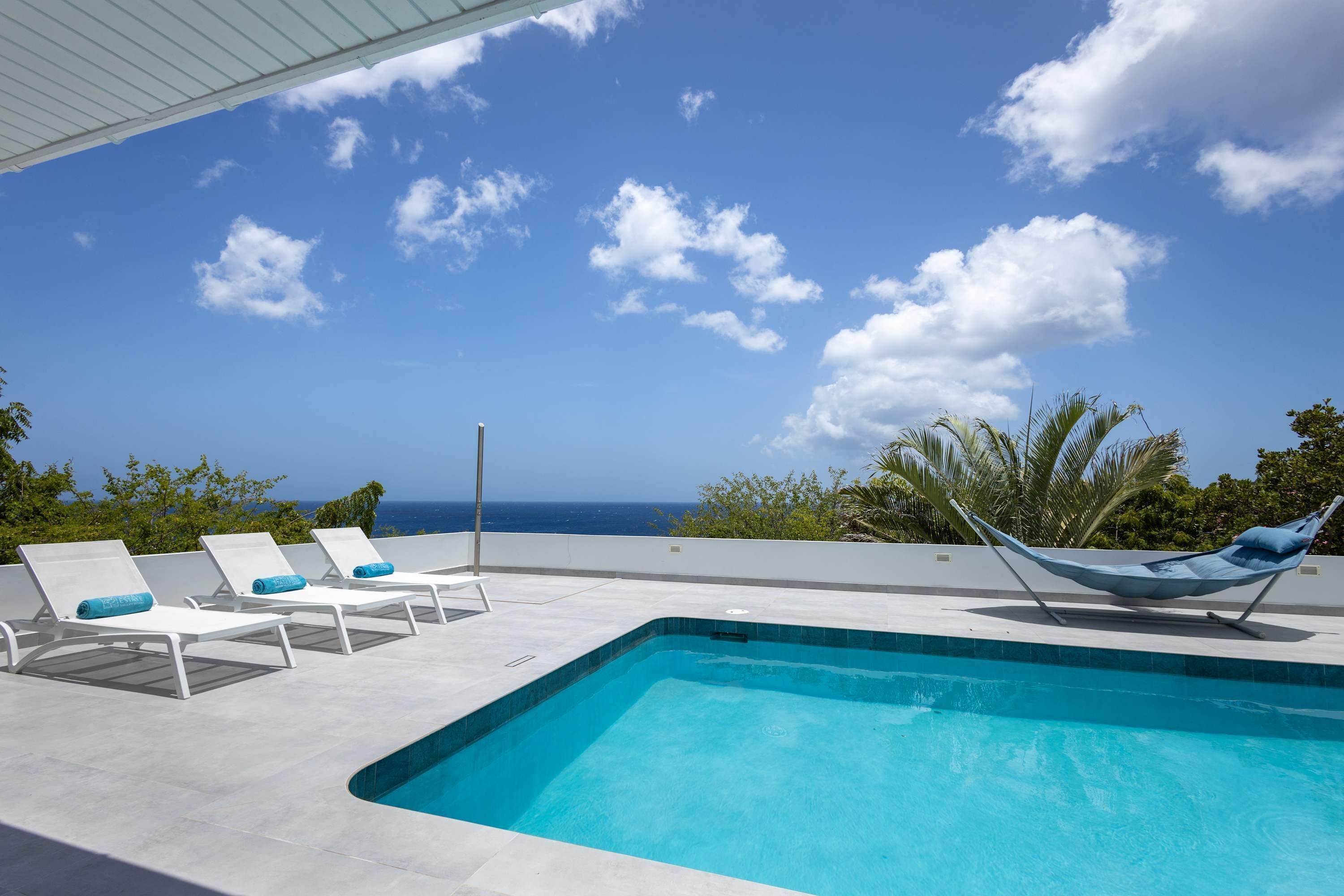A pool area with lounge chairs and a hammock, overlooking a body of water.
