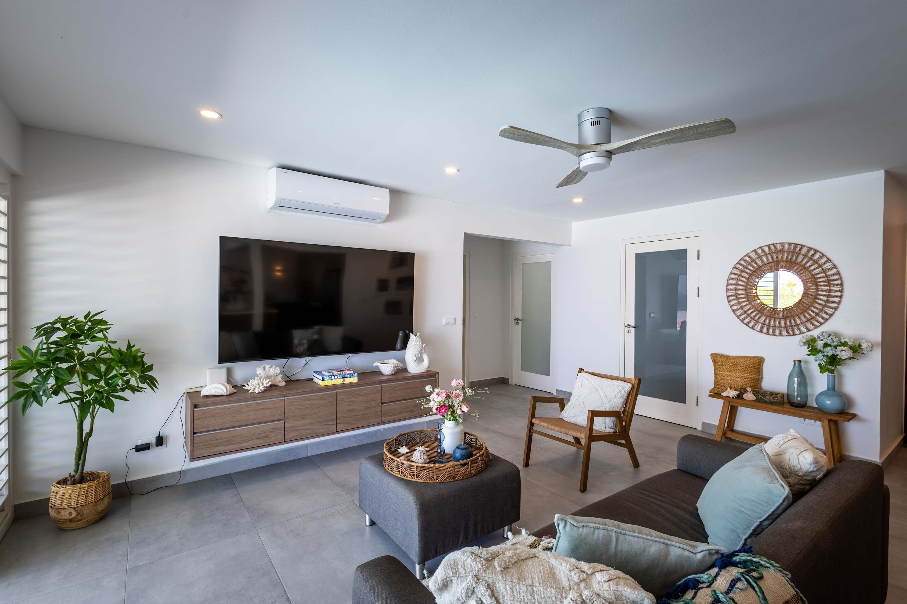 A modern living room with a flat-screen TV, a ceiling fan, a large window, and a dining area.