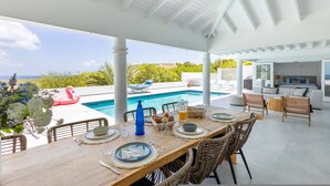 A covered outdoor dining area with a pool, wicker furniture, and a view of the ocean. - 270 Ocean Views From Private Pool Sun Terrace (St. Marie)