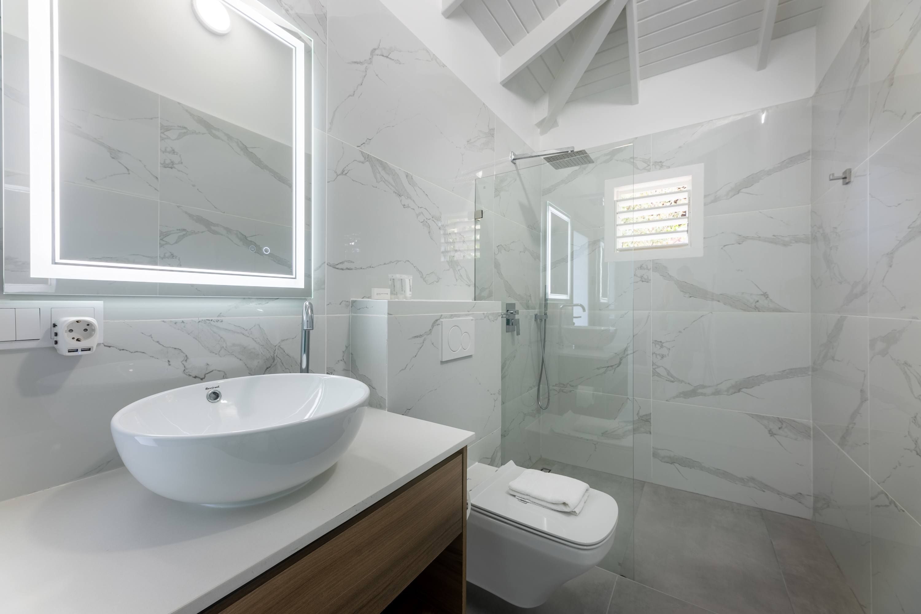 A modern bathroom with a large oval sink, a glass shower enclosure, and marble-patterned walls.