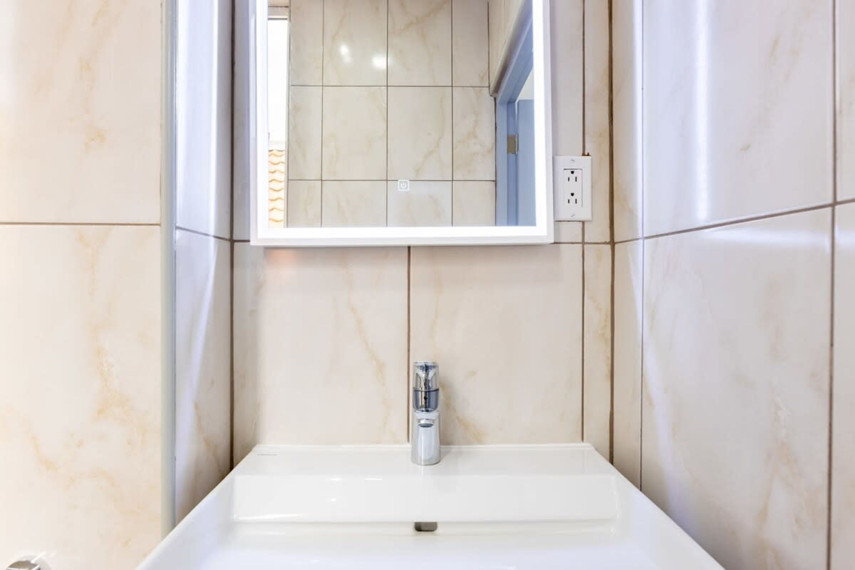 A bathroom with a white sink, a mirror, and a tiled wall.