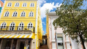 Un edificio amarillo llamado 'La Casa Amarilla' con un balcón y un escaparate que dice 'The Yellow House'.