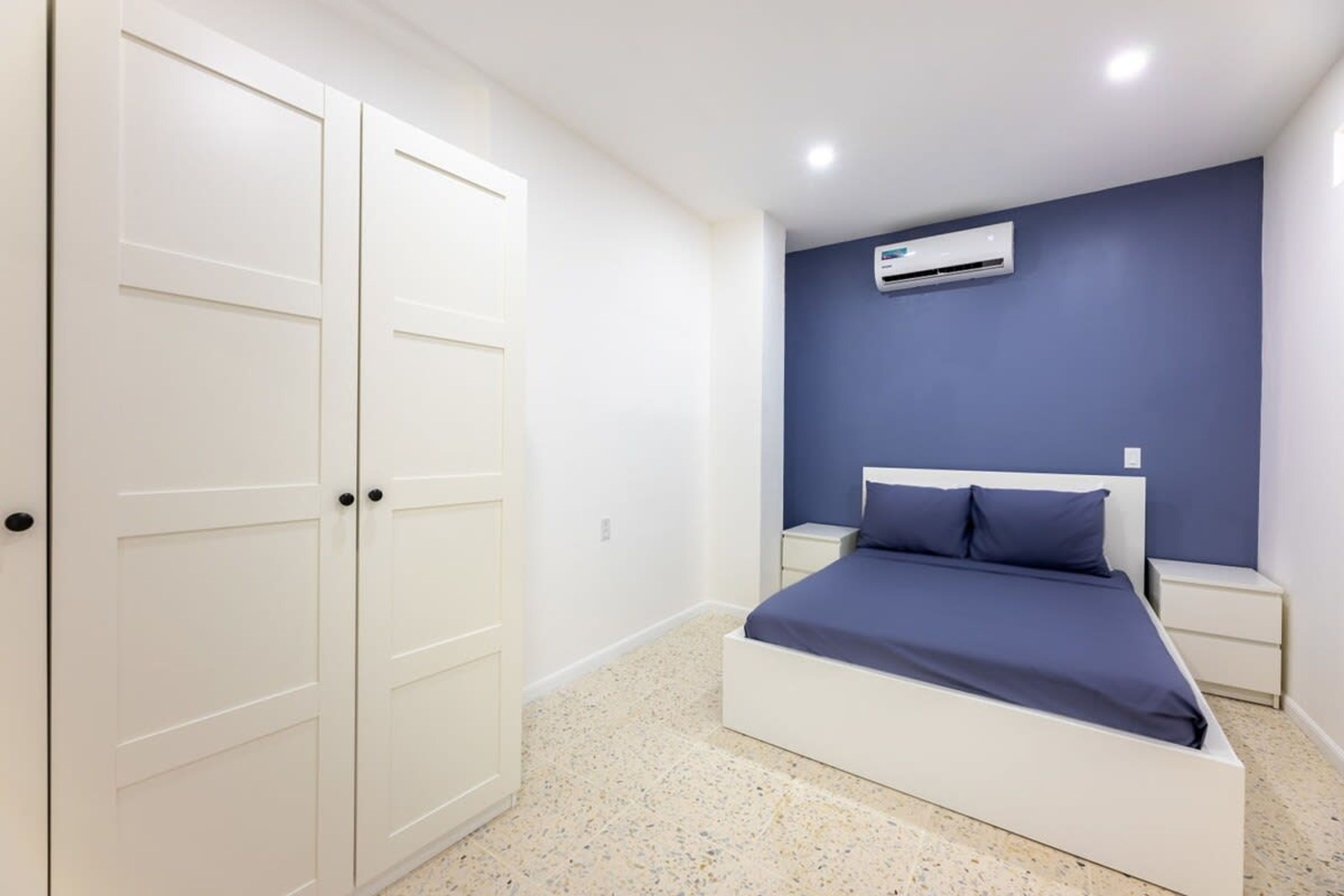 A bedroom with a bed, white wardrobe, and an air conditioning unit on the wall.