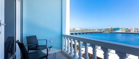 A balcony with a view of the sea, a table with chairs, and a potted plant.