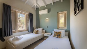 Une chambre avec deux lits simples, une petite table de chevet, un appareil de climatisation et une fenêtre avec des rideaux.