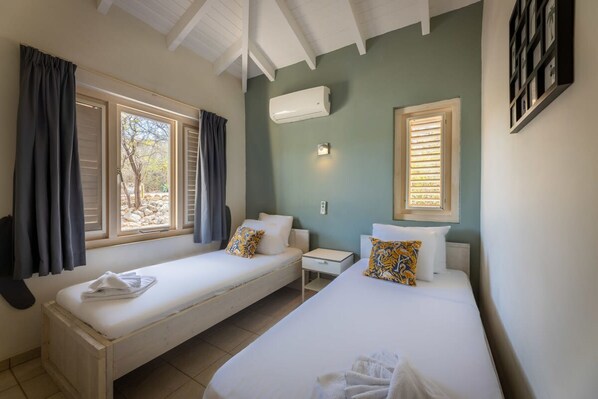 A room with two single beds, a small bedside table, an air conditioning unit, and a window with curtains. - Villa Aquatic Bliss - Infinity Pool Ocean View (St. Marie)