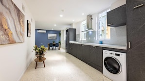 Une cuisine moderne dotée d’un lave-linge intégré, de meubles de rangement aux couleurs sombres et d’un coin repas à l’arrière-plan.