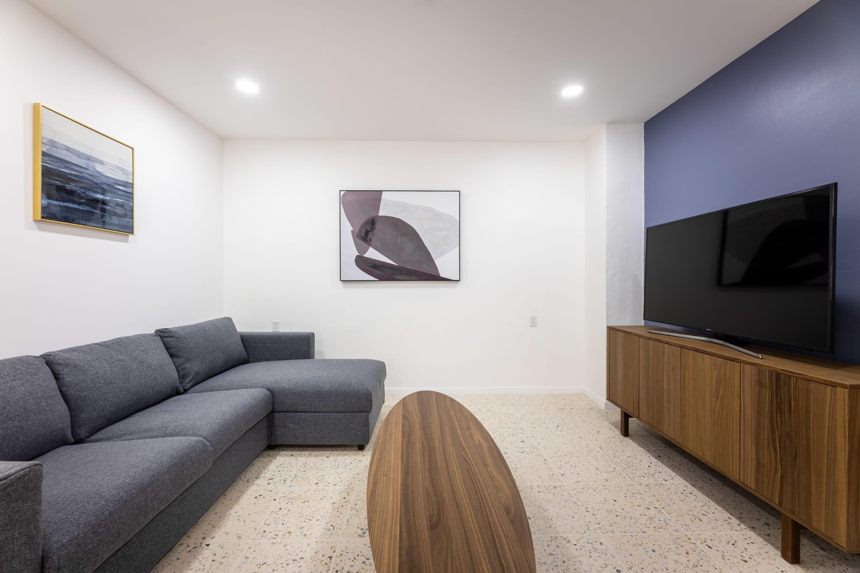 Una sala de estar moderna con un sofá seccional gris, una mesa de centro de madera, un televisor de pantalla plana sobre un mueble de madera y arte abstracto en las paredes.