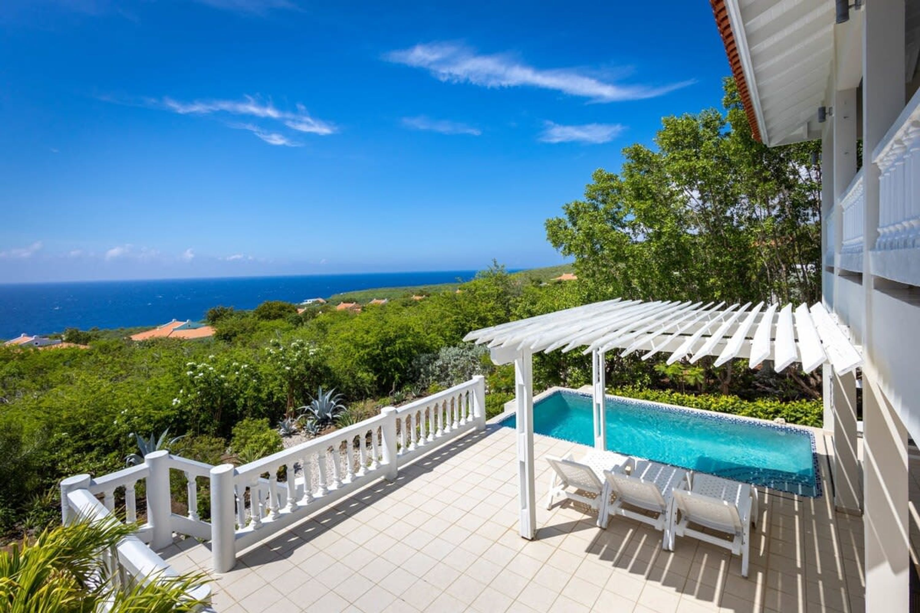 Un espace piscine agrémenté d’une pergola, de rampes blanches et offrant une vue sur l’océan.