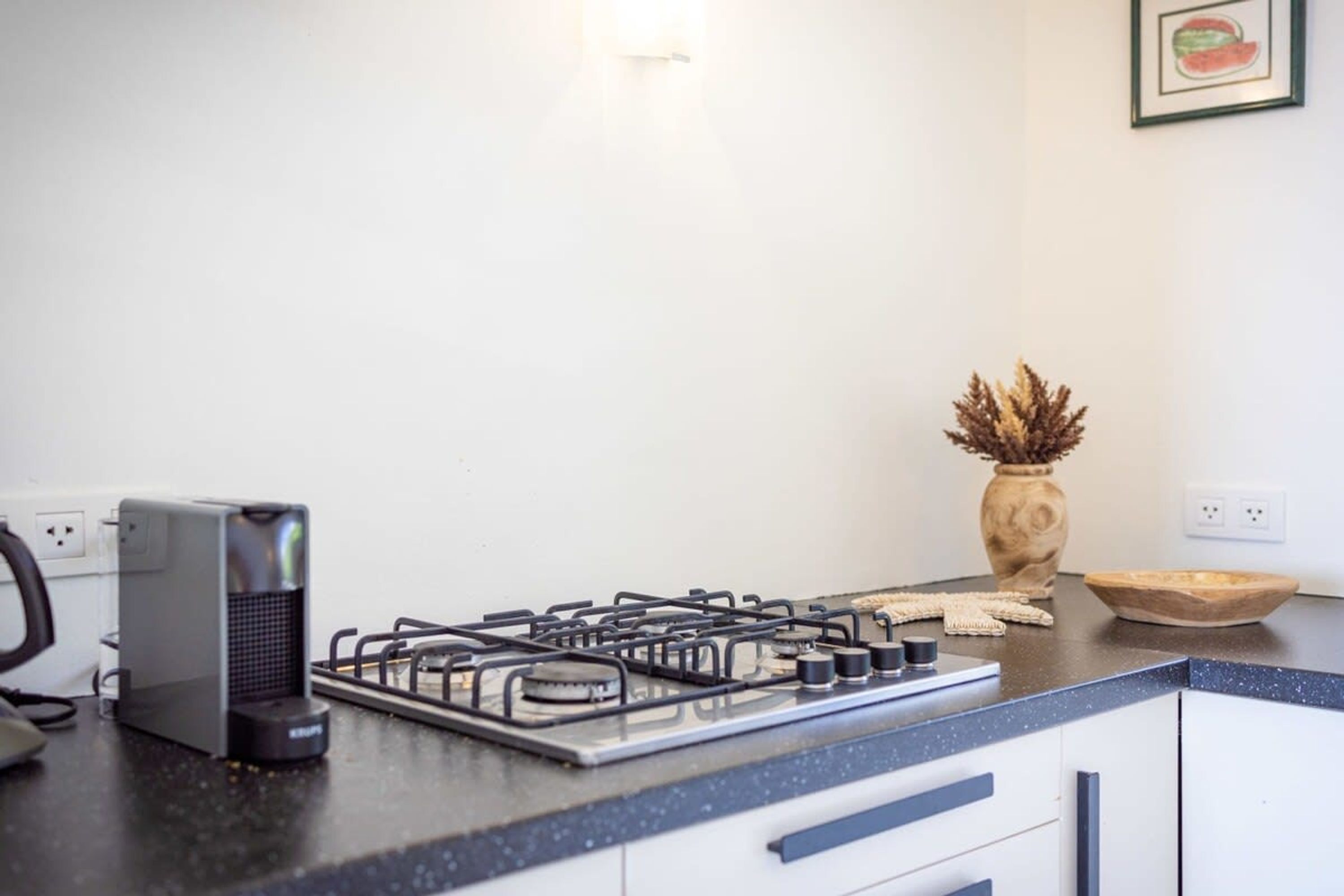 A kitchen with a gas stove, a coffee maker, and a vase with dried plants.