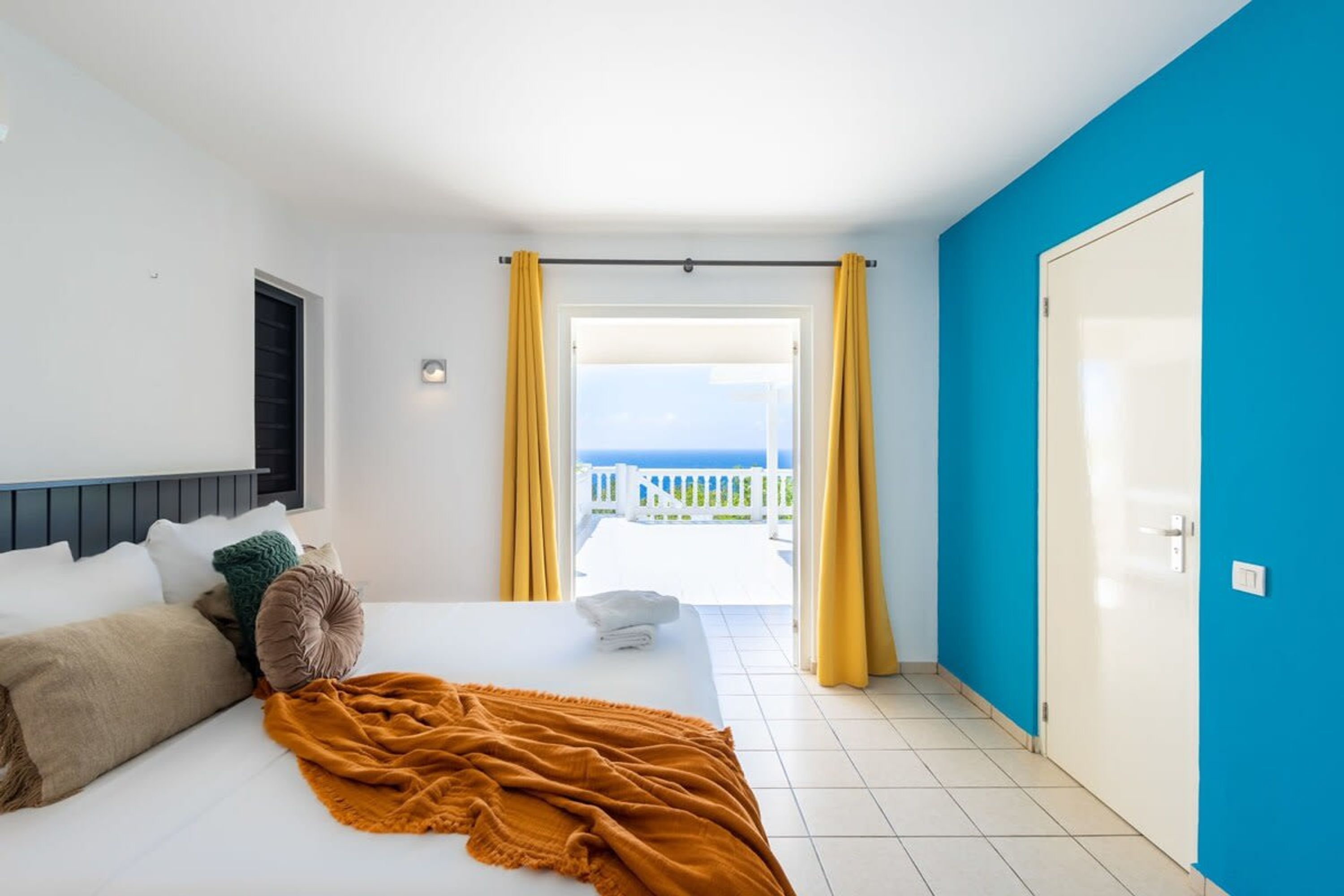 Une chambre d’hôtel avec un lit, une vue sur la mer, un balcon et un mur bleu.