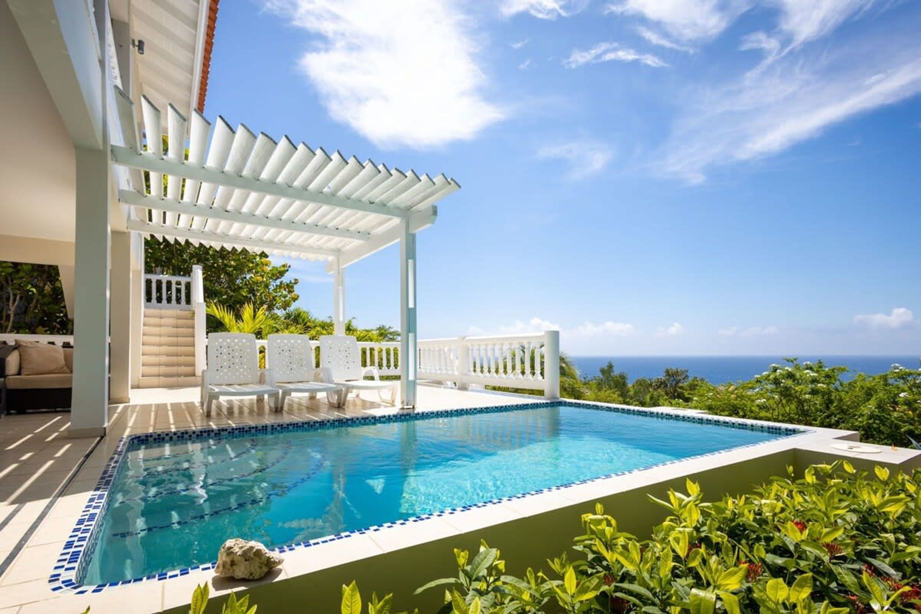 Ein Pool mit weißem Pergola, Liegestühlen und Blick auf den Ozean.