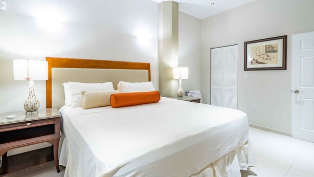 A hotel room with a large bed, two bedside tables, a nightstand, a lamp, a framed picture, and a closet. - Fabulous Chic Apartment Filled w Natural Light at Famous Handelskade (Willemstad)
