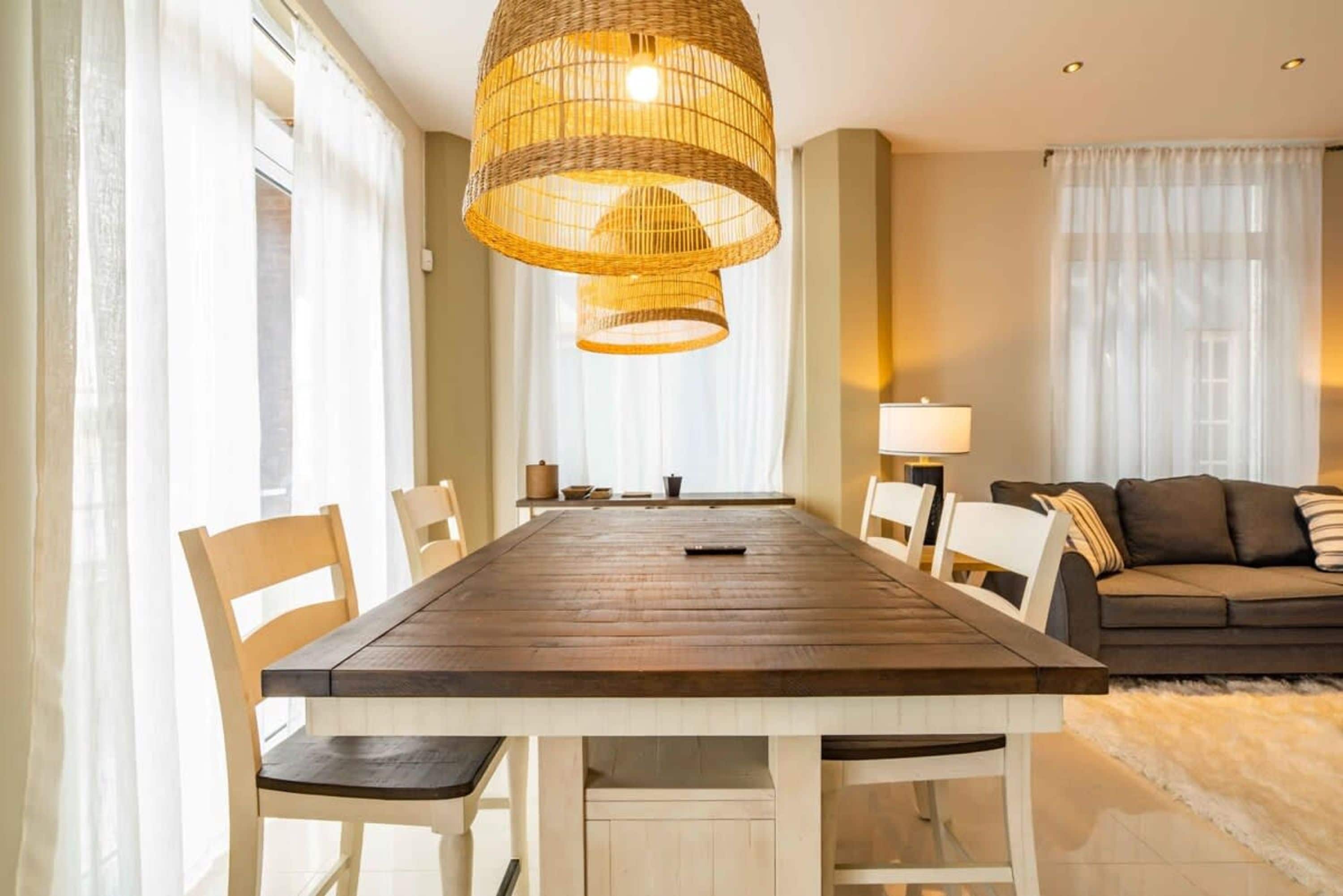Comedor con mesa de madera, sillas blancas y una lámpara colgante de fibras naturales.