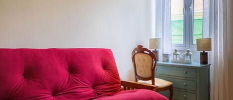 A room with a red sofa, a wooden chair, a blue dresser, and a window with curtains.