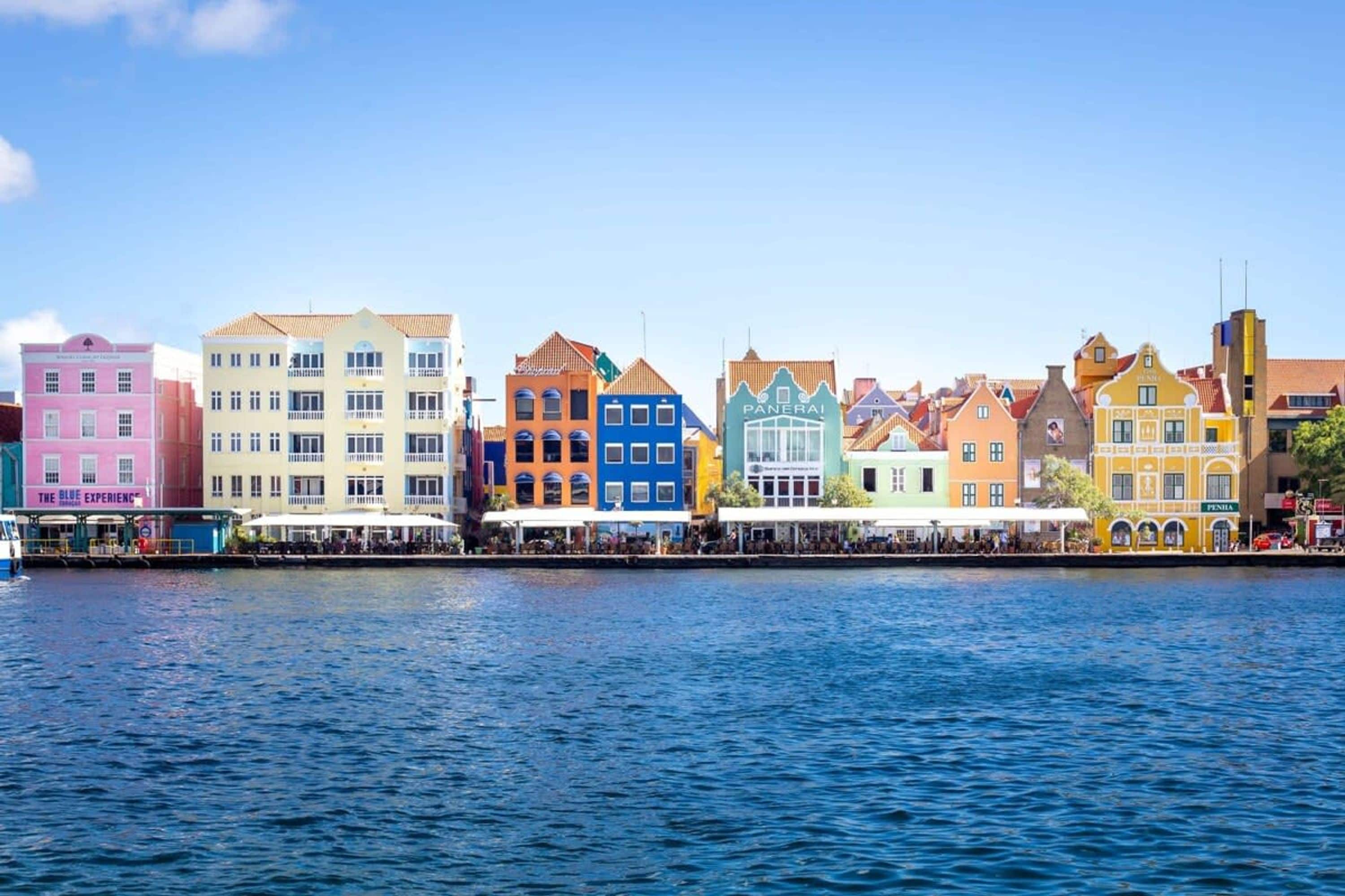 Un frente marítimo con edificios coloridos, incluyendo un edificio rosa con el letrero "The Blue Experience".