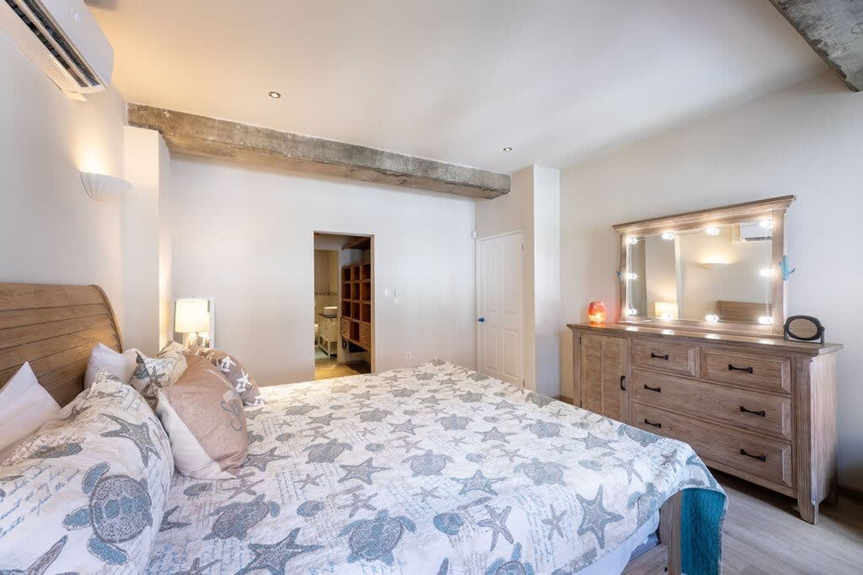 A bedroom with a bed, dresser, and a mirror with lights.