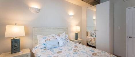 A bedroom with a bed, two bedside lamps, a nightstand with a drawer, a mirror, and a door.