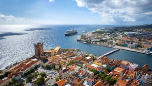 A coastal town with a prominent tall building, a marina with a cruise ship, and a colorful waterfront area. - Chic Historic Townhouse in City Centre Willemstad (Willemstad)