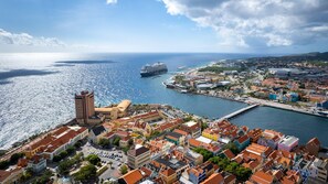 Une ville côtière qui se distingue par un grand immeuble imposant, un port de plaisance où est amarré un navire de croisière, et une zone riveraine aux couleurs vives.